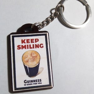 May include: A brown and white keychain with a picture of a glass of Guinness beer with a smiling face on the top. The text on the keychain reads "Keep Smiling" and "Guinness is good for you".