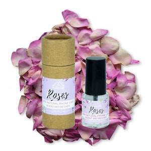 May include: Two bottles of rose scented phone case refresher. One bottle is in a cardboard tube with a pink and white label that says "MMORE Roses 100% Natural Phone Case Scent Refresher www.mmore.net". The other bottle is clear with a black cap and a pink and white label that says "Roses 100% Natural Phone Case Scent Refresher www.mmore.net". Both bottles are surrounded by pink rose petals.