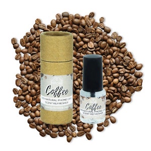 May include: Two bottles of coffee-scented phone case refresher. The bottles are brown and clear with a white label that says "Coffee 100% Natural Phone Case Scent Refresher" and "www.mmore.net". The bottles are surrounded by coffee beans.