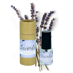 May include: A clear glass bottle with a black cap and a white label that reads "Lavender 100% Natural Phone Case Scent Refresher www.mmore.net". The bottle is sitting on a brown cardboard tube with a white label that reads "Lavender 100% Natural Phone Case Scent Refresher www.mmore.net". There are purple lavender flowers in the background.