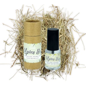 May include: A brown cardboard tube and a clear glass bottle with a black cap. Both containers have a white label with the text "Alpine Hay 100% Natural Phone Case Scent Refresher www.mmore.net". The containers are sitting on a bed of dried grass.