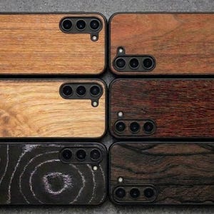 May include: Six rectangular smartphone cases arranged in two columns, each featuring a distinct wood grain finish. The cases display various natural wood tones ranging from light tan to dark brown and black, with cutouts for three camera lenses.