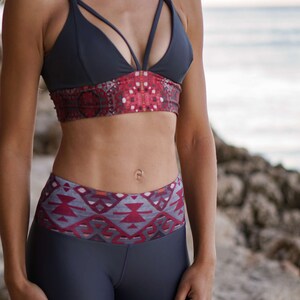 Pode incluir: Uma mulher vestindo um suti&atilde; esportivo cinza escuro com uma faixa estampada em vermelho e cinza e leggings cinza escuros combinando com uma cintura estampada em vermelho e cinza.