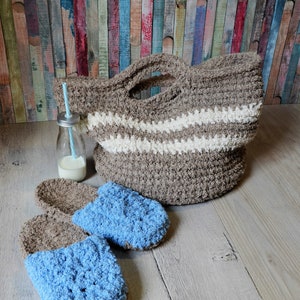 May include: Two pairs of fuzzy crocheted slippers, one pair is brown and the other is blue. A brown crocheted tote bag with white stripes sits on a wooden surface.