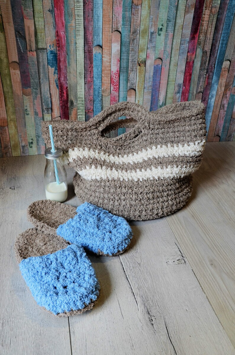 May include: Two pairs of fuzzy crocheted slippers, one pair is brown and the other is blue. A brown crocheted tote bag with white stripes sits on a wooden surface.
