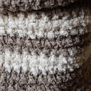 May include: A close-up of a brown and white fluffy rug with a textured surface. The rug is made of soft, looped fibers.