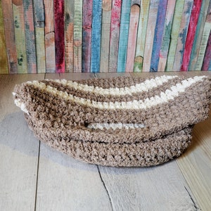 May include: A brown and white striped bath mat with a fluffy texture. The mat is folded in half and lying on a wooden floor.
