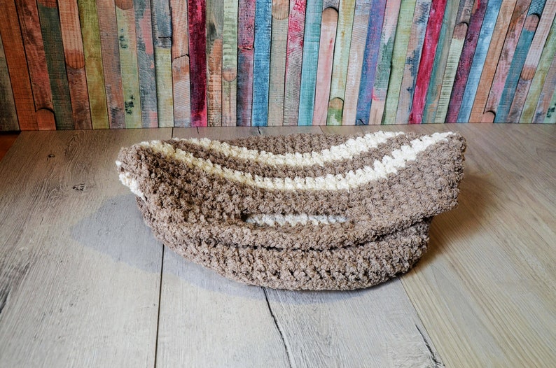 May include: A brown and white striped bath mat with a fluffy texture. The mat is folded in half and lying on a wooden floor.