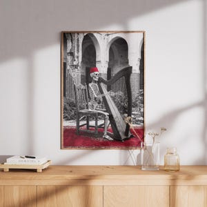 May include: A framed black and white print featuring a skeleton wearing a red fez and playing a harp. The skeleton sits on a wooden chair on a red rug, with an arched building in the background. The print has a wooden frame.