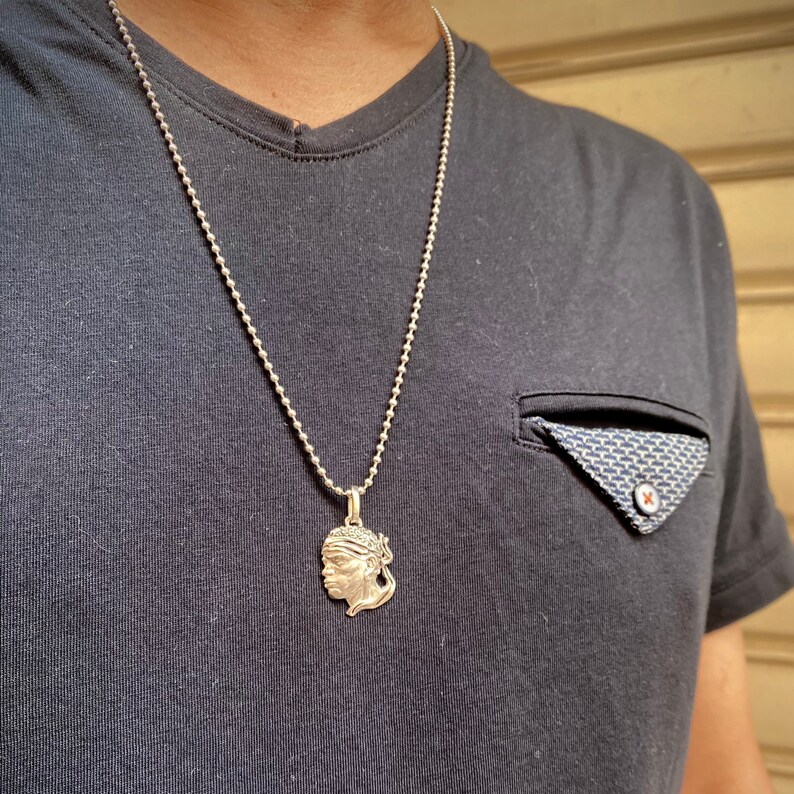 Puede incluir: Un collar de cadena de plata con un colgante de plata que presenta un perfil detallado de la cara de una persona.