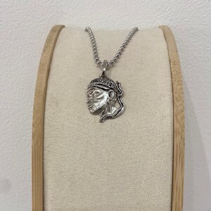 Puede incluir: Un collar de plata con un colgante que presenta un perfil detallado de una persona con un turbante. El colgante est&aacute; en una cadena de plata.