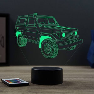 Op de afbeelding: Een 3D-geprint nachtlampje in de vorm van een groene omtrek van een vintage Toyota Land Cruiser. Het lampje staat op een zwarte basis en heeft een afstandsbediening.