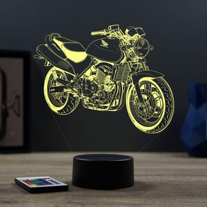 Op de afbeelding: Een 3D-geprint nachtlampje in de vorm van een Honda-motorfiets. Het licht is geel en de motorfiets is zwart omlijnd. Het lampje staat op een zwarte basis.