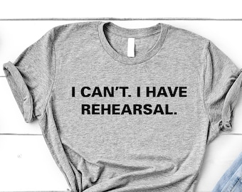 Op de afbeelding: Een grijs T-shirt met de tekst "I CAN'T. I HAVE REHEARSAL." in zwart gedrukt.