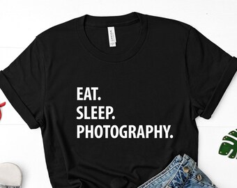 May include: Black t-shirt with white text that reads "Eat. Sleep. Photography."
