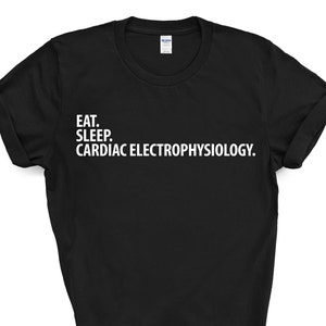 Può includere: T-shirt nera con testo bianco: "EAT. SLEEP. CARDIAC ELECTROPHYSIOLOGY." La maglietta girocollo ha le maniche arrotolate. Il testo è in un semplice font senza grazie. Un capo casual.