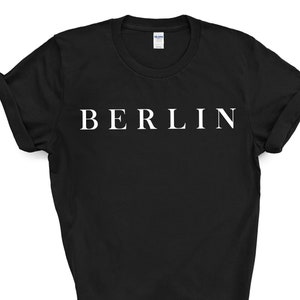 May include: Black t-shirt with the word "BERLIN" printed in white, centered across the chest. The sleeves are cuffed. The shirt is a solid color and appears to be made of cotton.