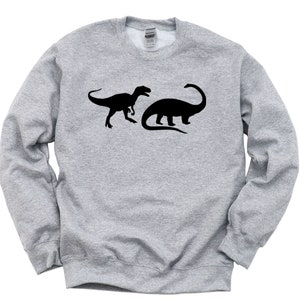 Peut inclure: Un sweat-shirt gris avec une silhouette noire de Tyrannosaurus Rex et de Brachiosaurus.