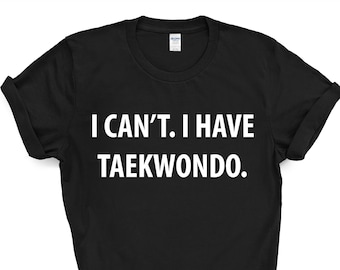 Op de afbeelding: Zwart t-shirt met de witte tekst "I CAN'T. I HAVE TAEKWONDO." Het shirt heeft opgerolde mouwen en een ronde hals. De tekst staat in het midden van de voorkant van het shirt.