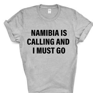 Könnte beinhalten: Ein graues T-Shirt mit schwarzem Text, der "Namibia is calling and I must go." lautet.