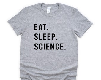 Op de afbeelding: Een lichtgrijs t-shirt met de tekst "EAT. SLEEP. SCIENCE." in vette, zwarte hoofdletters. Het t-shirt heeft een ronde hals en korte mouwen.
