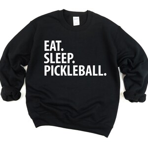 K&ouml;nnte beinhalten: Schwarzer Pullover mit wei&szlig;em Text, der "Essen. Schlafen. Pickleball." lautet.