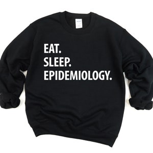 K&ouml;nnte beinhalten: Schwarzer Pullover mit wei&szlig;em Text, der "Essen. Schlafen. Epidemiologie." lautet.