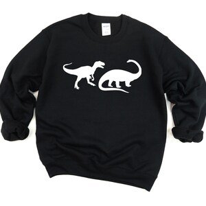 K&ouml;nnte beinhalten: Schwarzer Pullover mit einer wei&szlig;en Silhouette von zwei Dinosauriern auf der Vorderseite.
