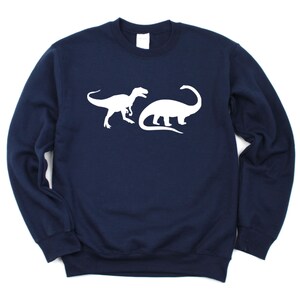 K&ouml;nnte beinhalten: Ein marineblauer Pullover mit einer wei&szlig;en Silhouette eines Tyrannosaurus Rex und eines Brachiosaurus.