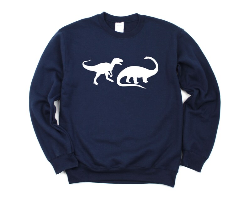 K&ouml;nnte beinhalten: Ein marineblauer Pullover mit einer wei&szlig;en Silhouette eines Tyrannosaurus Rex und eines Brachiosaurus.
