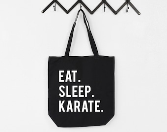 May include: Black canvas tote bag with white text that reads "Eat. Sleep. Karate."