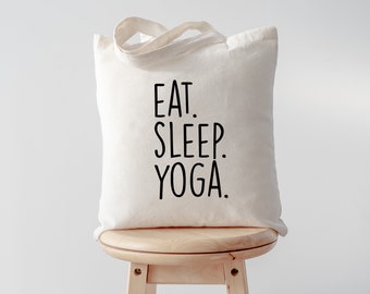May include: A white canvas tote bag with black text that reads "EAT. SLEEP. YOGA."