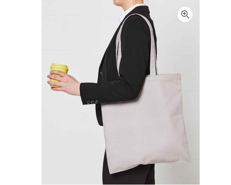 May include: A person holding a yellow reusable coffee cup and carrying a large, light grey tote bag with long straps.