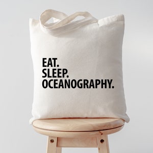 Può includere: Una borsa di tela bianca con testo nero che dice "Eat. Sleep. Oceanography."