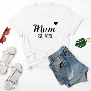 May include: White t-shirt with black text that reads "Mum Est. 2020" with a small black heart.