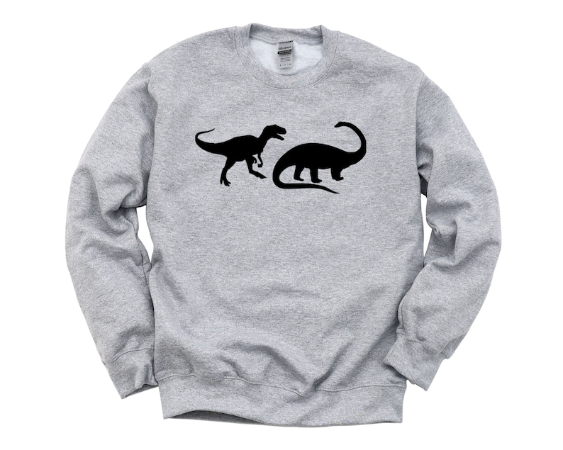 K&ouml;nnte beinhalten: Ein graues Sweatshirt mit einer schwarzen Silhouette eines Tyrannosaurus Rex und eines Brachiosaurus.