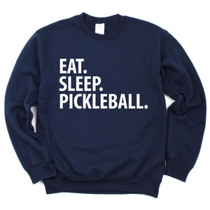 K&ouml;nnte beinhalten: Ein marineblauer Pullover mit dem Aufdruck "EAT. SLEEP. PICKLEBALL." in wei&szlig; auf der Vorderseite.