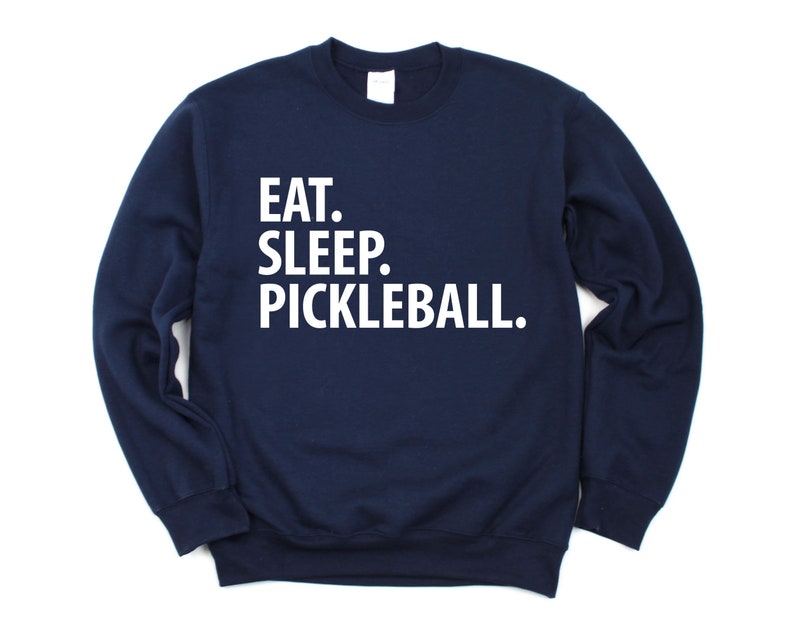 K&ouml;nnte beinhalten: Ein marineblauer Pullover mit dem Aufdruck "EAT. SLEEP. PICKLEBALL." in wei&szlig; auf der Vorderseite.