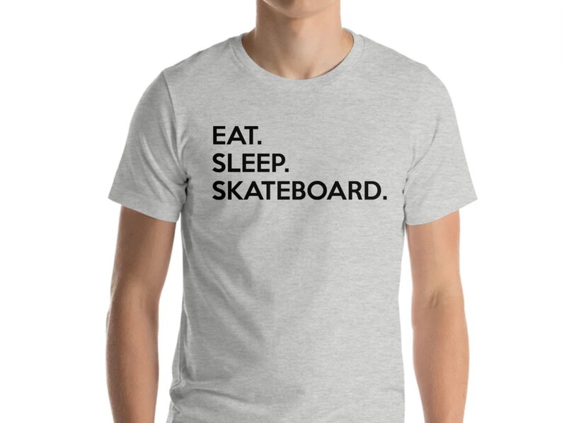 K&ouml;nnte beinhalten: Ein graues T-Shirt mit dem Text "EAT. SLEEP. SKATEBOARD." in Schwarz gedruckt.