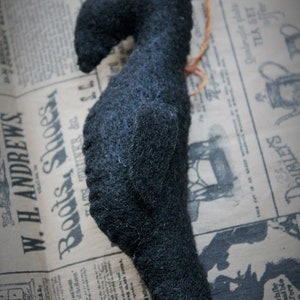 May include: A black felt crow with a red bead for an eye. The crow is sitting on a piece of old newspaper.