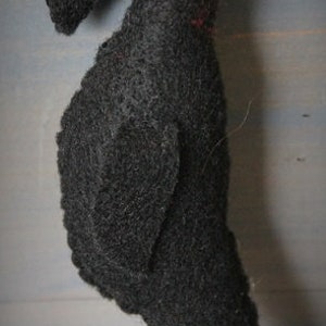 May include: Black felt crow ornament with red button eyes. The crow is hanging from a brown string.