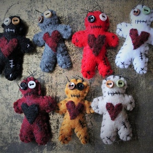 May include: Eight felt voodoo dolls with different colored bodies and black stitching. Each doll has a red felt heart and button eyes.
