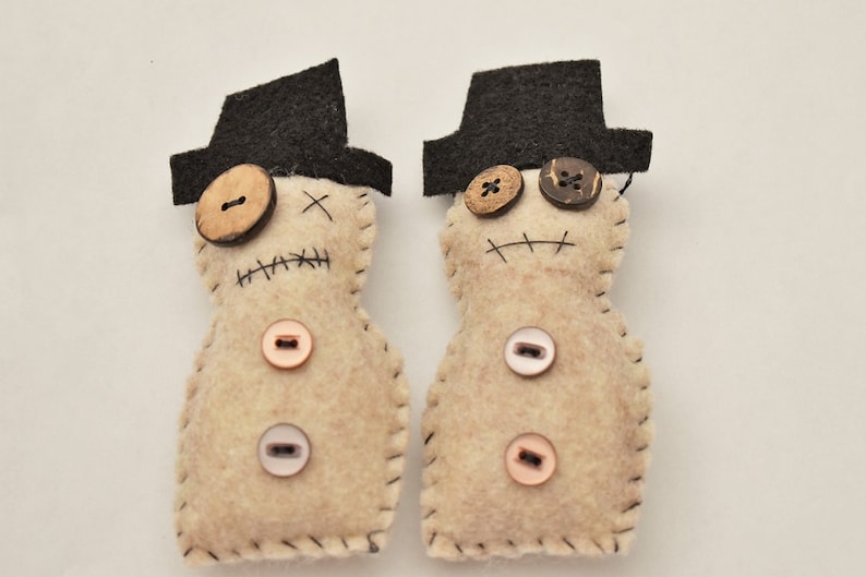 May include: Two felt dolls with black hats and button eyes. The dolls have stitched mouths and are decorated with various buttons.
