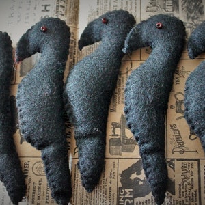 May include: Five black felt bird ornaments with red bead eyes. The birds are arranged in a row on a patterned surface.