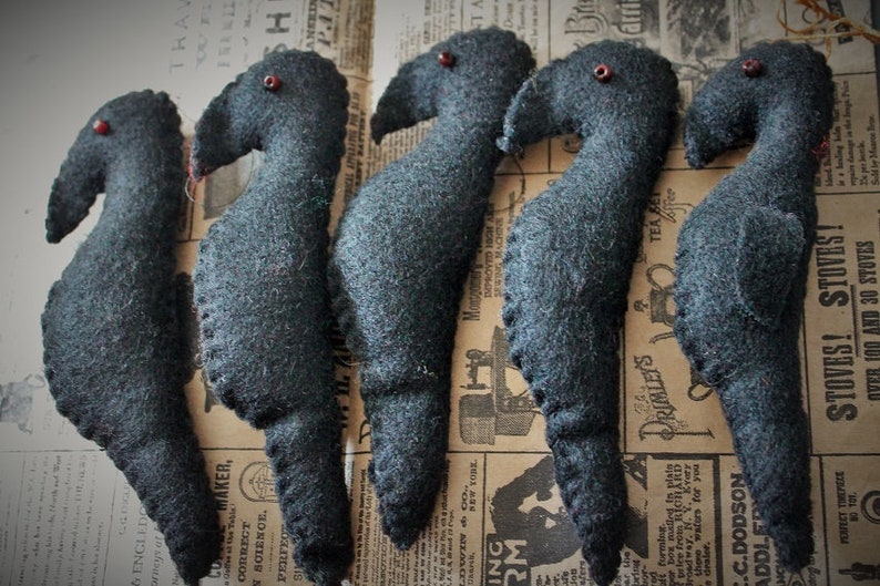 May include: Five black felt bird ornaments with red bead eyes. The birds are arranged in a row on a patterned surface.