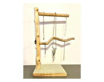 May include: A wooden jewelry stand with a natural, light brown finish. The stand has two branches, one horizontal and one curved, for hanging necklaces and bracelets. The stand has a square base.