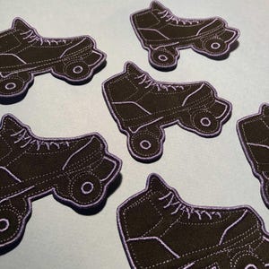Peut inclure: Cinq patchs brodés de patins à roulettes noirs et blancs. Les patchs sont soulignés de fil violet.