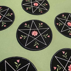 May include: Six black embroidered iron-on patches with a white pentagram and pink flowers. The patches are circular and have a white outline.