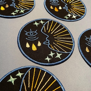 Peut inclure: Cinq patchs brodés avec un motif de croissant de lune. La lune est soulignée de bleu et a un œil jaune et trois larmes jaunes. La lune est entourée de rayons de soleil jaunes et de trois étoiles blanches.