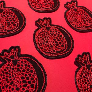 May include: Six red embroidered pomegranate patches on a red background. The pomegranates are outlined in black and have a detailed design.
